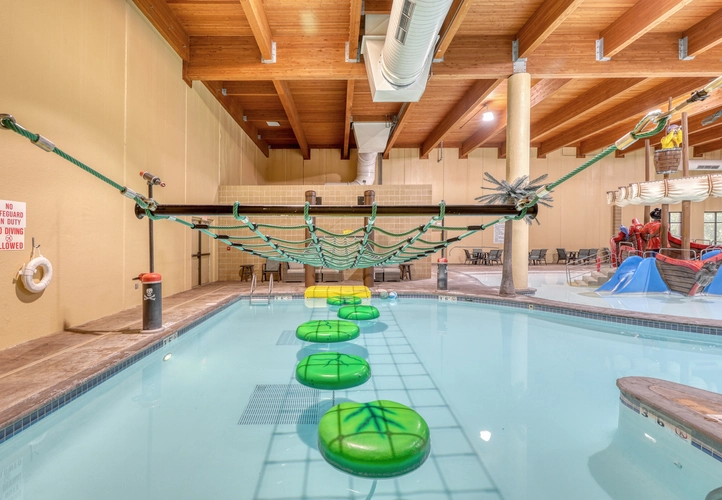 A pool obstacle course with floating fake lily pads and a rope net hanging above them.