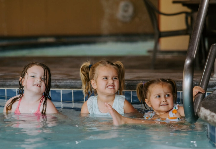 Three little girls sit on the steps to a pool.